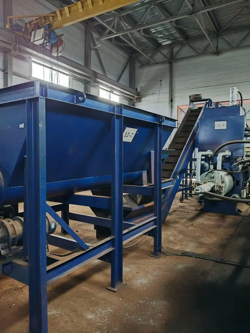 Large blue steel mixing hopper labelled 12-7 on a raised frame, with a yellow overhead gantry crane above it.